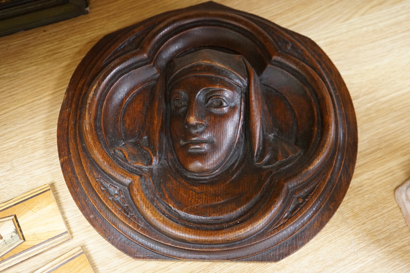 A pair of Gothic revival oak wall plaques, a Black Forest carved barometer, a Virgin and child figure, an IHS embroidered panel, two straw worked panels and a carved finial, barometer 47cm high
